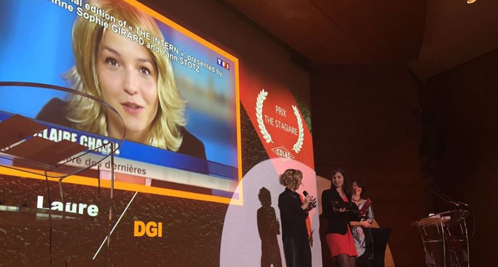 présentation de prix ou une cérémonie sur une scène. Un écran géant projette l'image d'une personnalité de la télévision