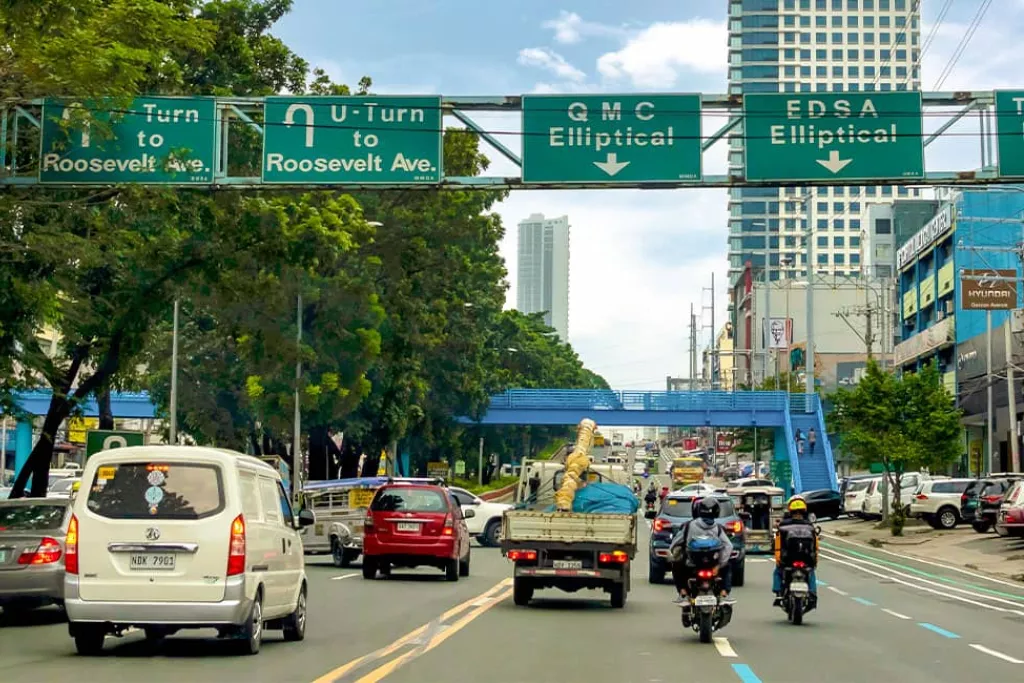 Circulation urbaine dense, panneaux routiers, bâtiments modernes en arrière-plan.