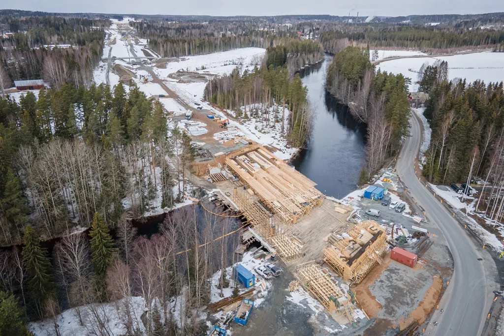 Chantier de construction d'un pont en bois au-dessus d'une rivière entourée par une forêt recouverte de neige