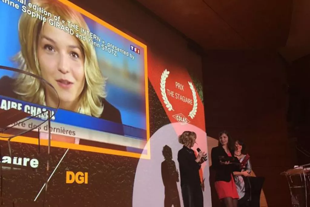 présentation de prix ou une cérémonie sur une scène. Un écran géant projette l'image d'une personnalité de la télévision