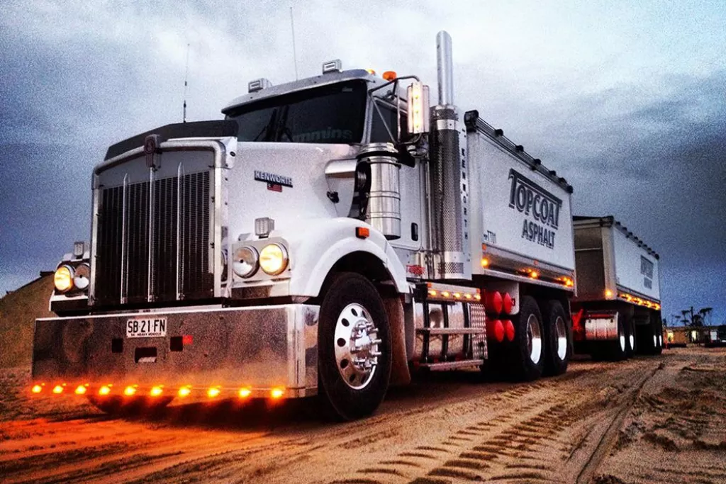Camion blanc transporteur sur un terrain sablonneux au crépuscule.