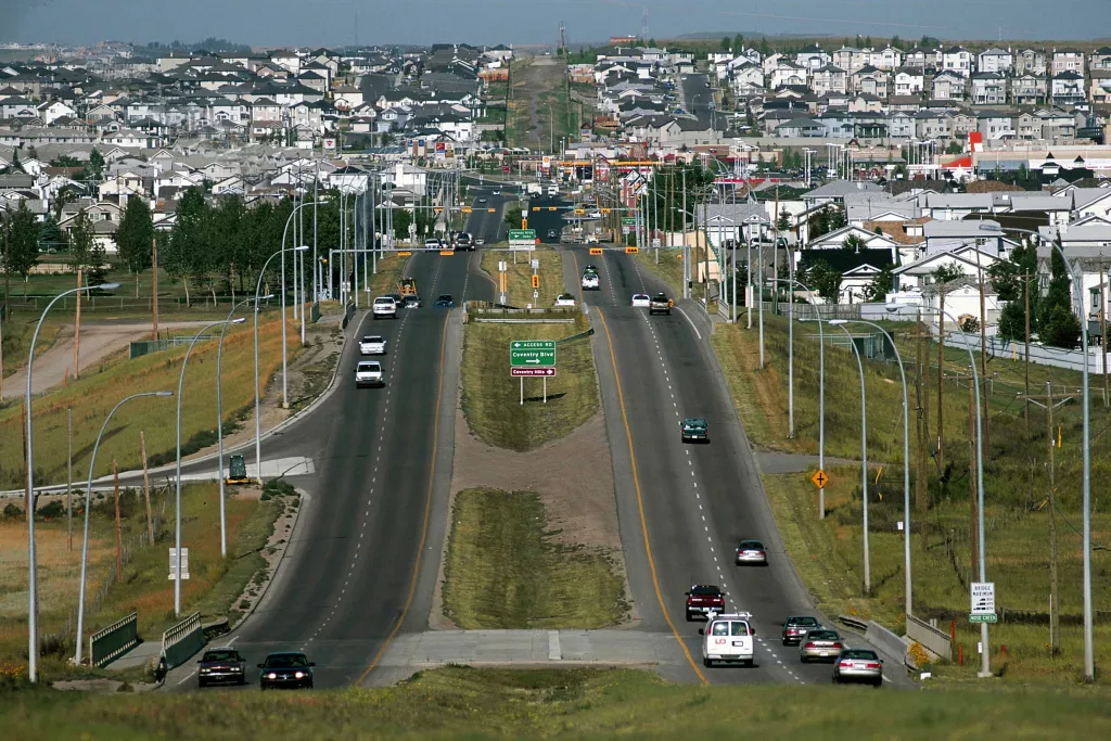  Route urbaine animée, voitures en mouvement, quartier résidentiel dense en arrière-plan.
