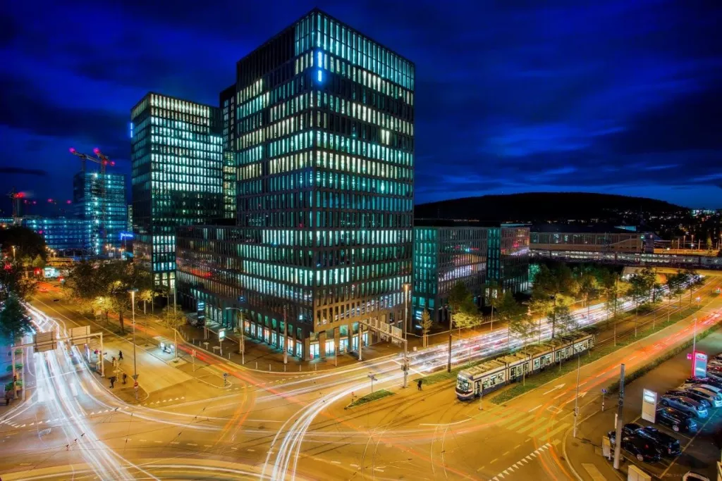 Ville nocturne moderne avec immeubles éclairés, traînées lumineuses de voitures, ambiance dynamique