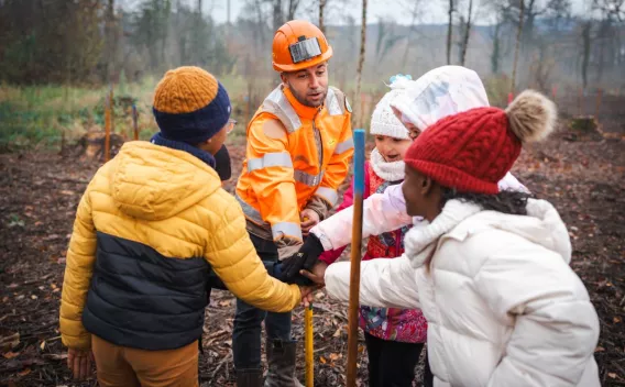 Chef de chantier et enfants réunis dans une forêt, main dans la main.