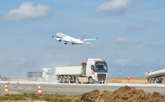 Un avion décolle au-dessus d’un chantier mobilisant les équipes Colas pour réhabiliter la piste 4 de Paris-Orly, un projet alliant performance technique et réduction significative de l’empreinte carbone.