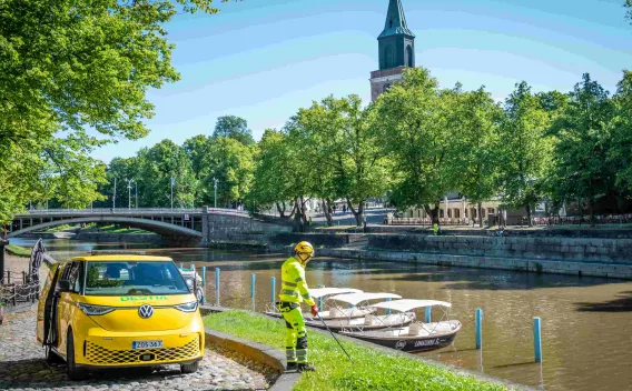 Agent d’entretien au bord de la rivière de Turku, avec véhicule d’intervention et pont en arrière-plan.