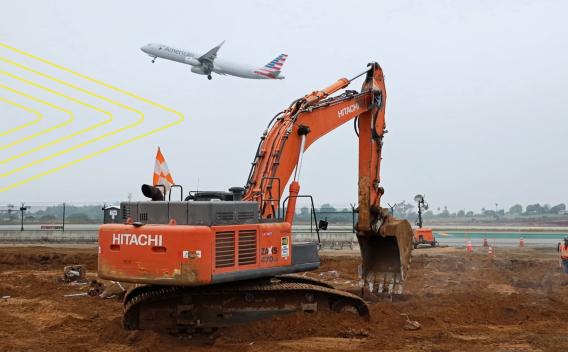 Pelle mécanique en activité sur un chantier aéroportuaire, avec un avion au décollage en arrière-plan