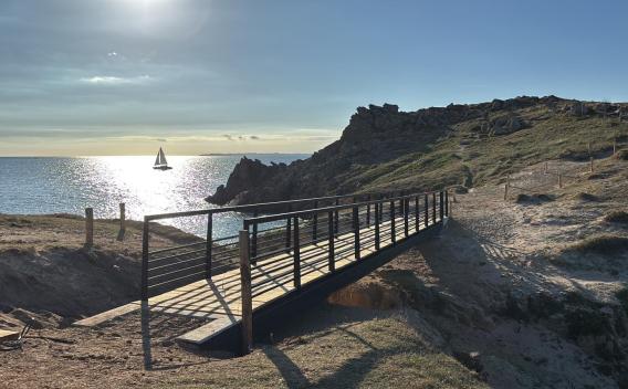 Passerelle côtière à Hoëdic avec vue sur l'océan et un voilier.
