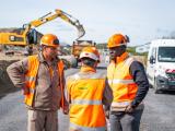Trois chefs de chantier Colas en discussion sur un chantier, engins de terrassement en arrière-plan.