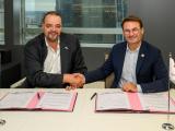 Deux représentants de Colas et de TotalEnergies se serrent la main après la signature d’un accord de partenariat, assis à une table où figurent les documents signés et les drapeaux des deux entreprises.