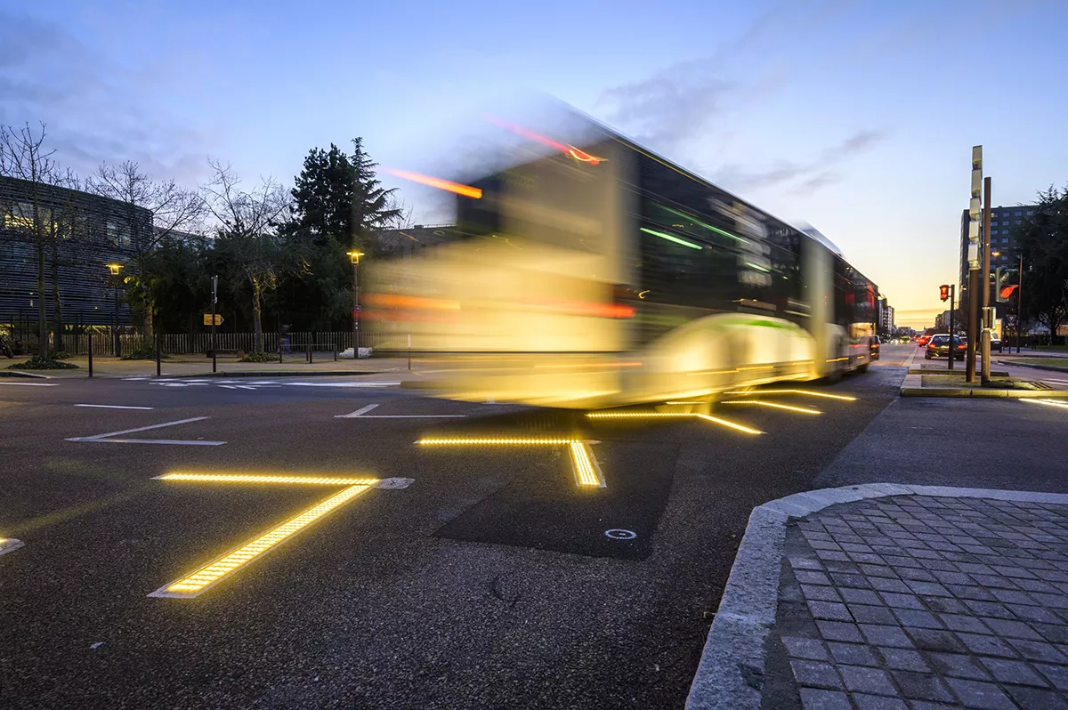 A dynamic urban scene where a bus crosses an intersection, creating a sensation of movement with a noticeable blur