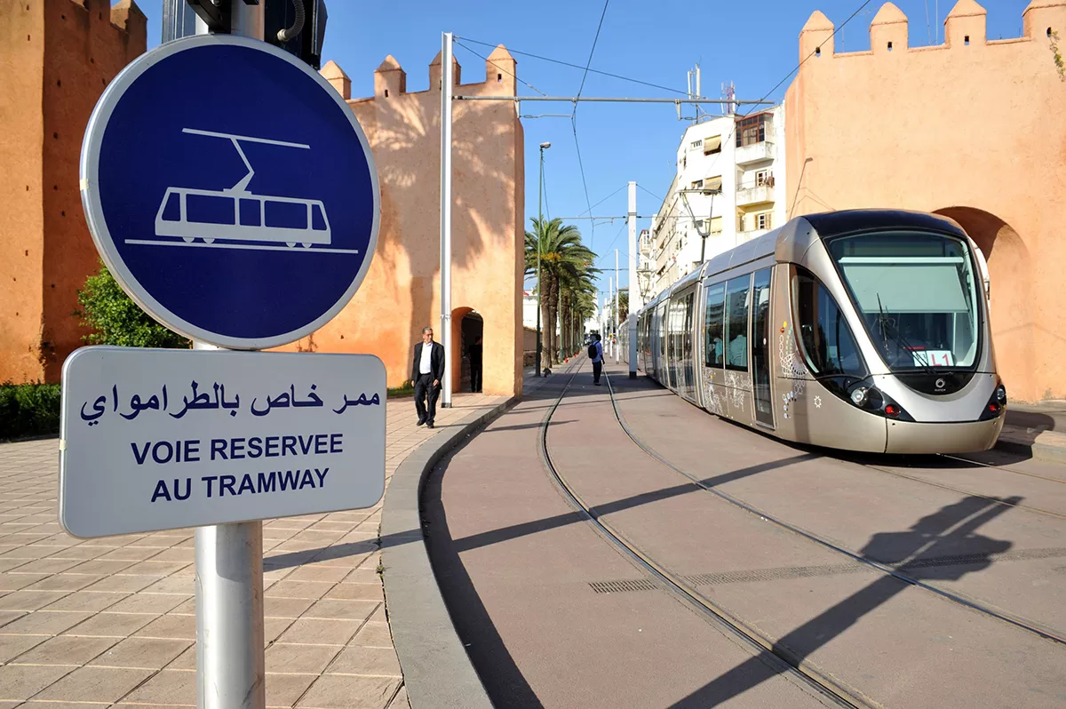 Tramway running on a reserved lane, with signs in French and Arabic, in a typical urban and architectural setting.