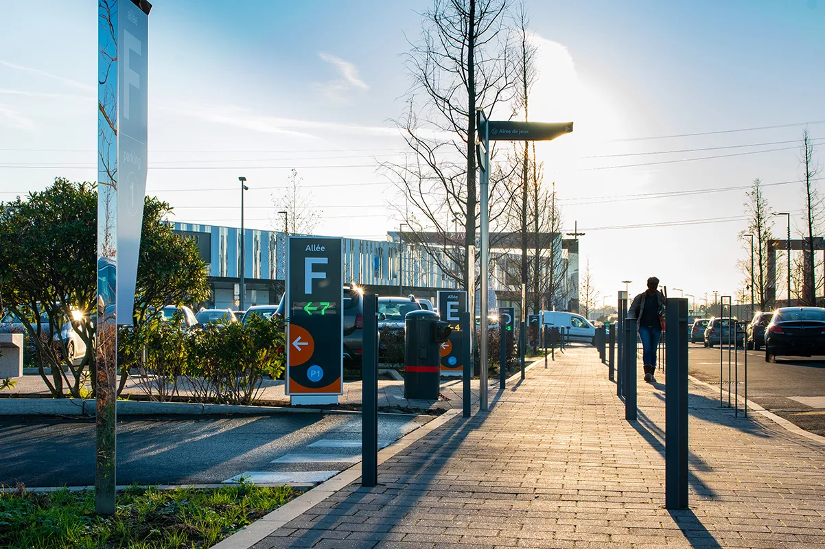 Alley in a parking lot and a man walking along a paved path under a clear sky.